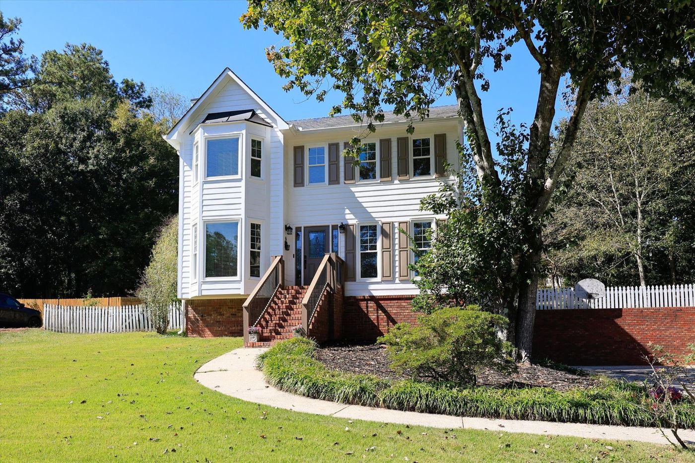 White two-story home with brick stairs and a shaded front lawn