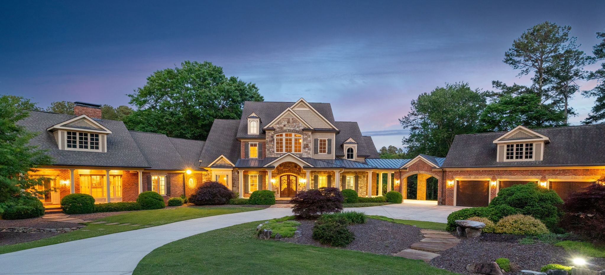 Brick and stone estate at twilight with every window lit